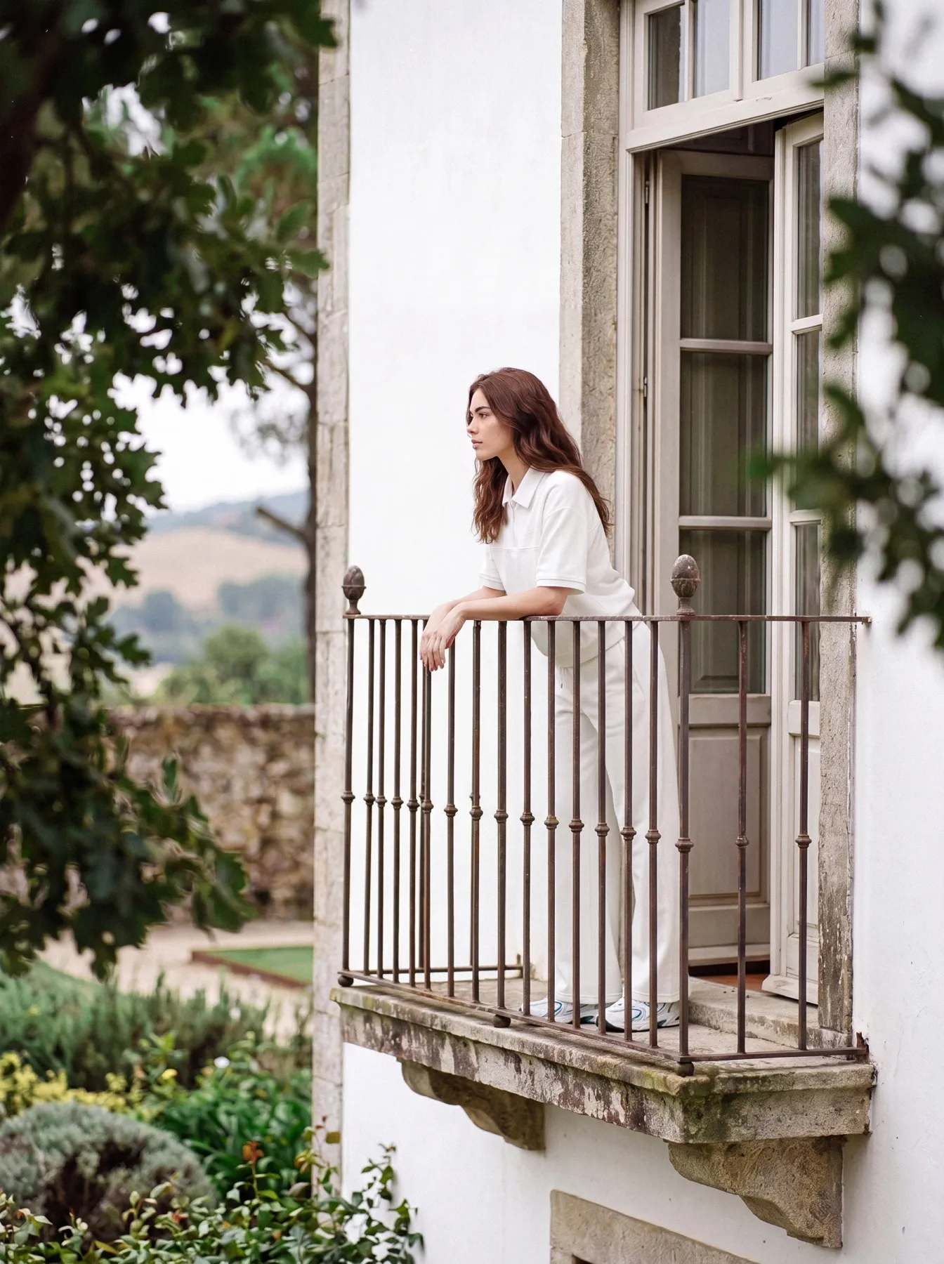 Model leaning on a wrought-iron balcony on the house’s white façade